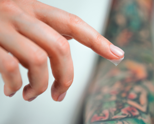 How to care for an infected tattoo. A finger with ointment hovers over a tattoo.