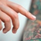 How to care for an infected tattoo. A finger with ointment hovers over a tattoo.