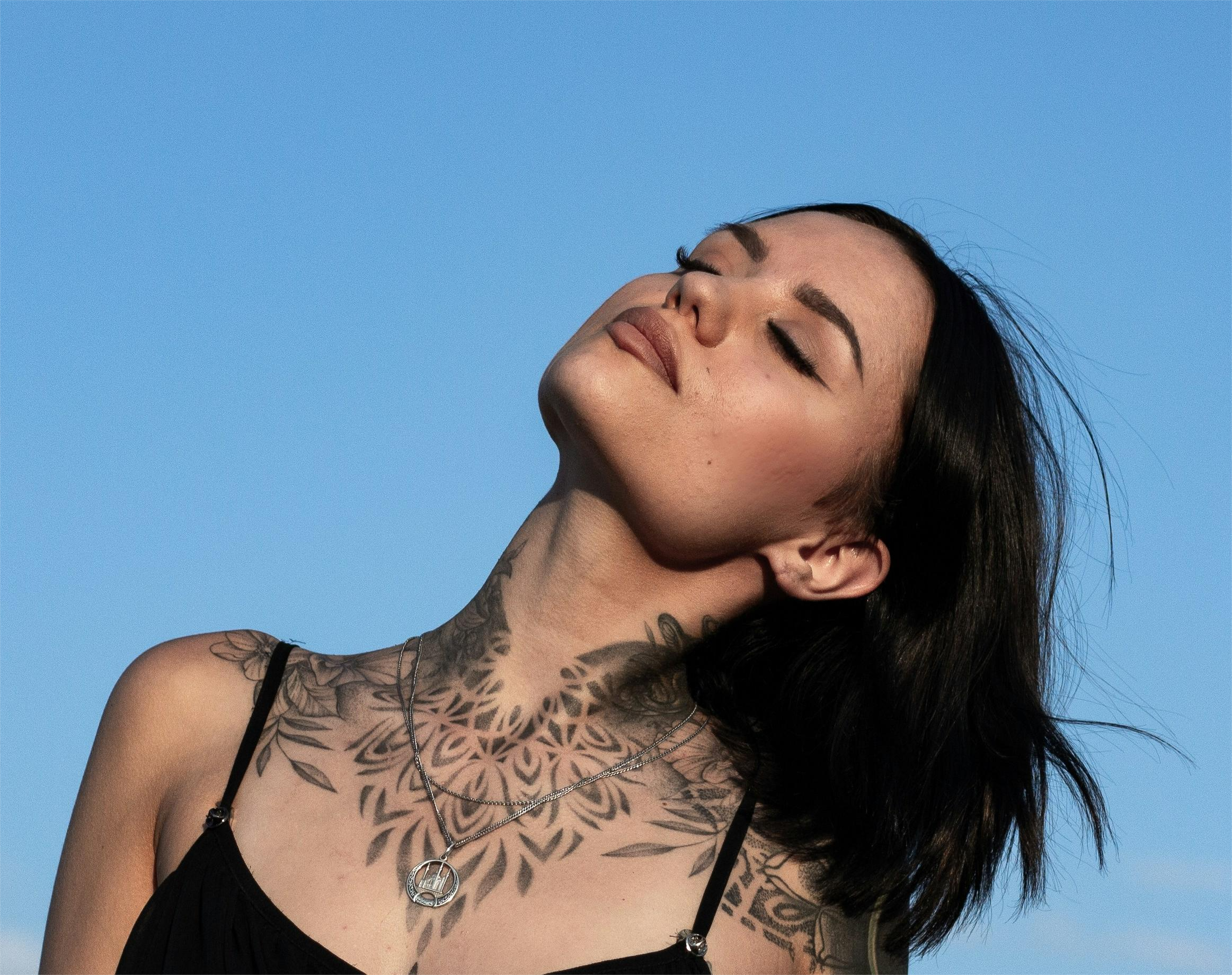 A tattooed woman turns her face up to the sun, answering the question if tattoos heal.