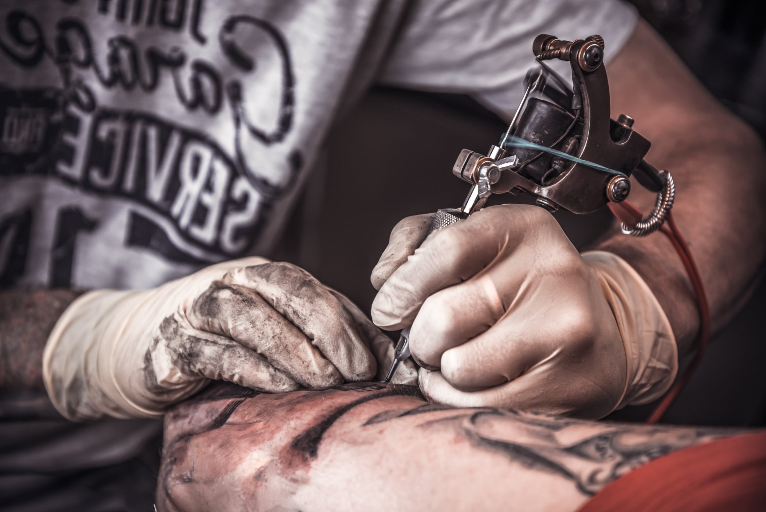 Close-up of a tattoo artist creating an intricate illustrative tattoo with fine lines and detailed shading.